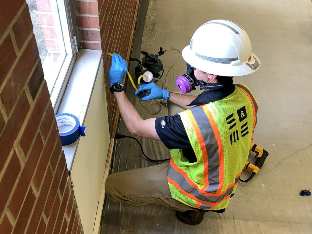 Technician sampling materials in wall with respirator